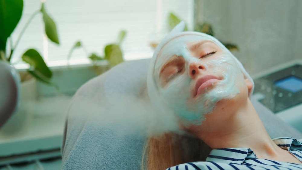 A woman in a spa rests as a facial steamer shoots steam toward her face.