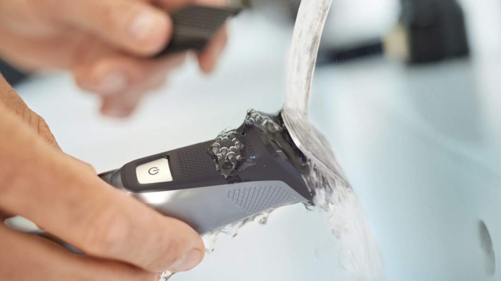 Person washing compact beard trimmer in a bathroom sink 