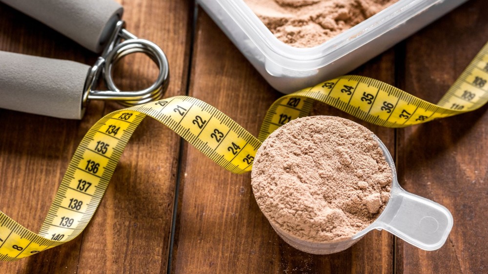 A cup of protein powder next to a measuring tape.