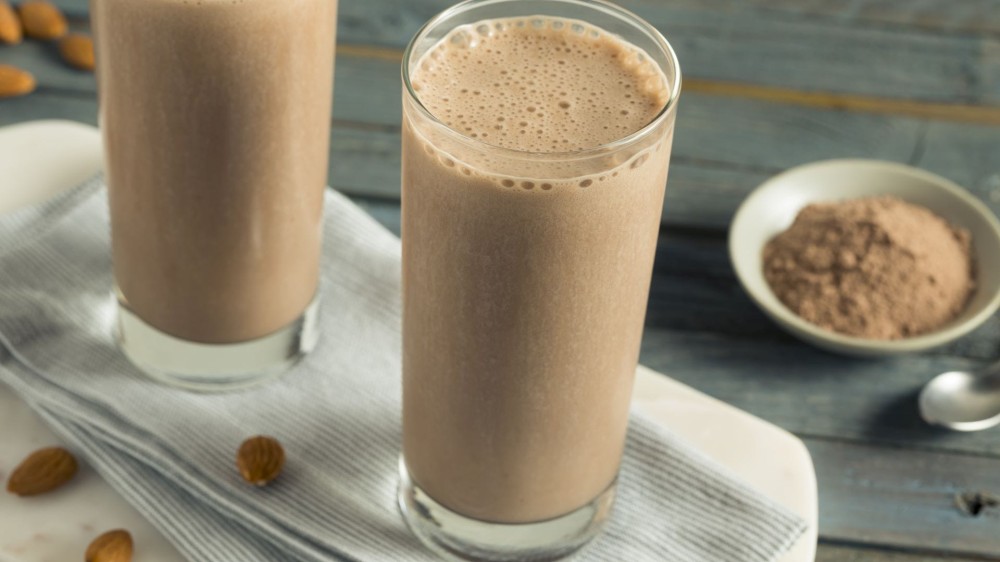 Two chocolate protein shakes next to a bowl of protein powder.