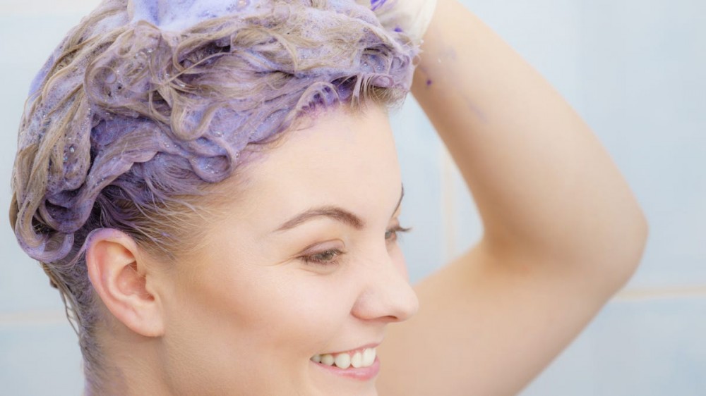 a woman scrubs her head with purple shampoo