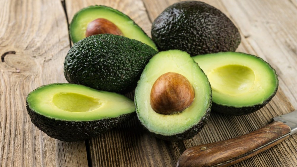 A wooden board filled with halved avocados and one knife.