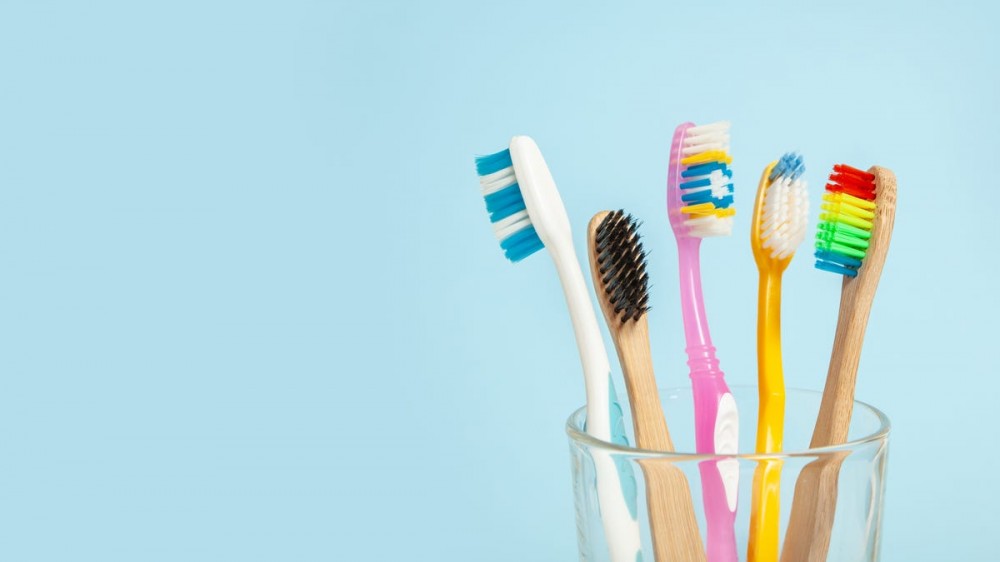 Colorful toothbrushes sit in a clear glass.