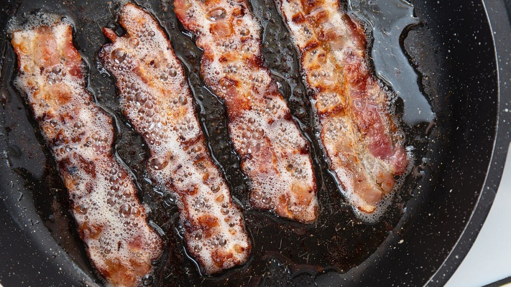 Bacon is cooking in grease in a pan.