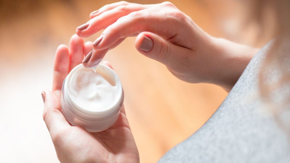 A person using a small container of moisturizer. 