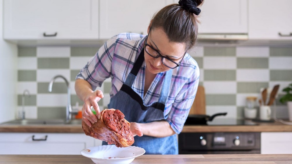 A woman looks at a piece of raw meat in a kitchen.