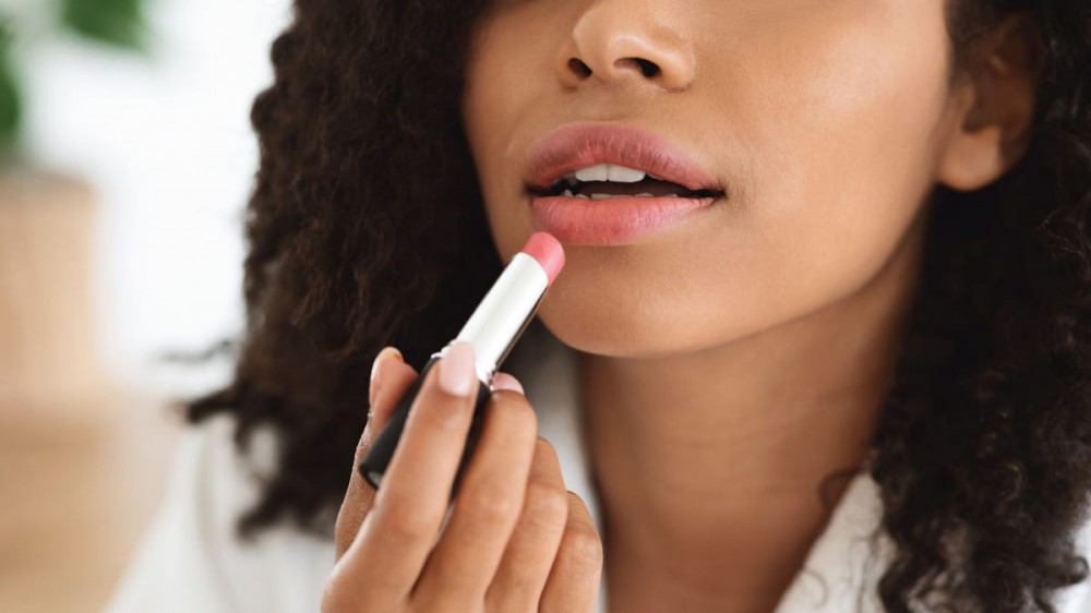 A woman applies pink lipstick to her lips.