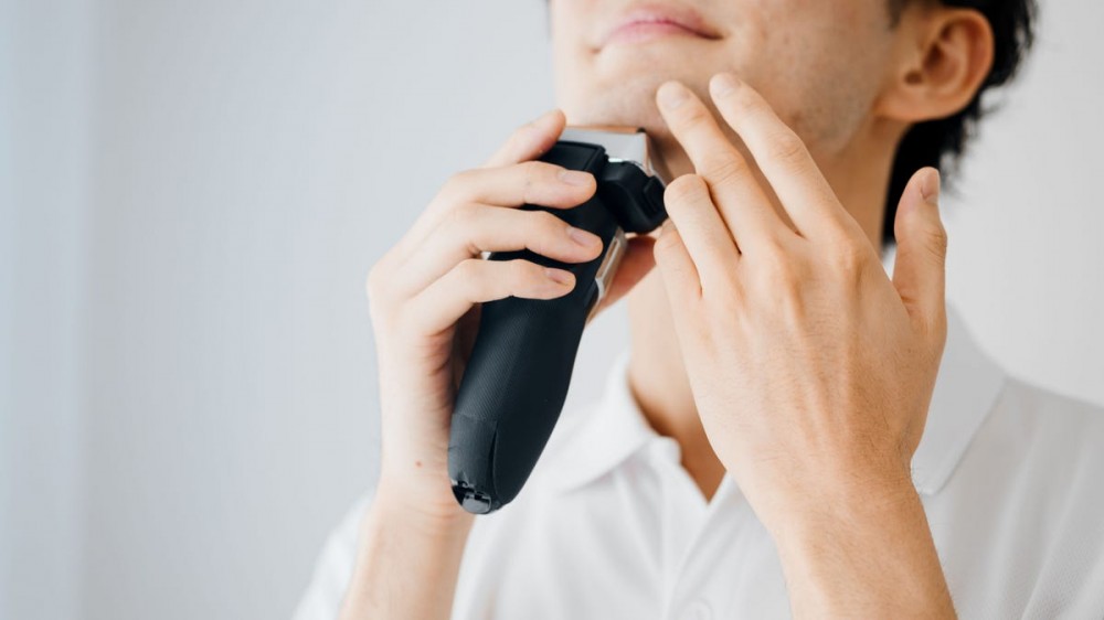 Young man shaving in the morning with an electric razor.