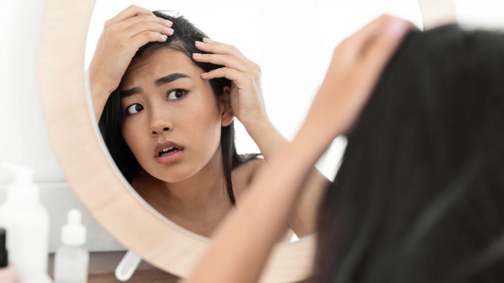 A woman examines her hairline in a mirror.