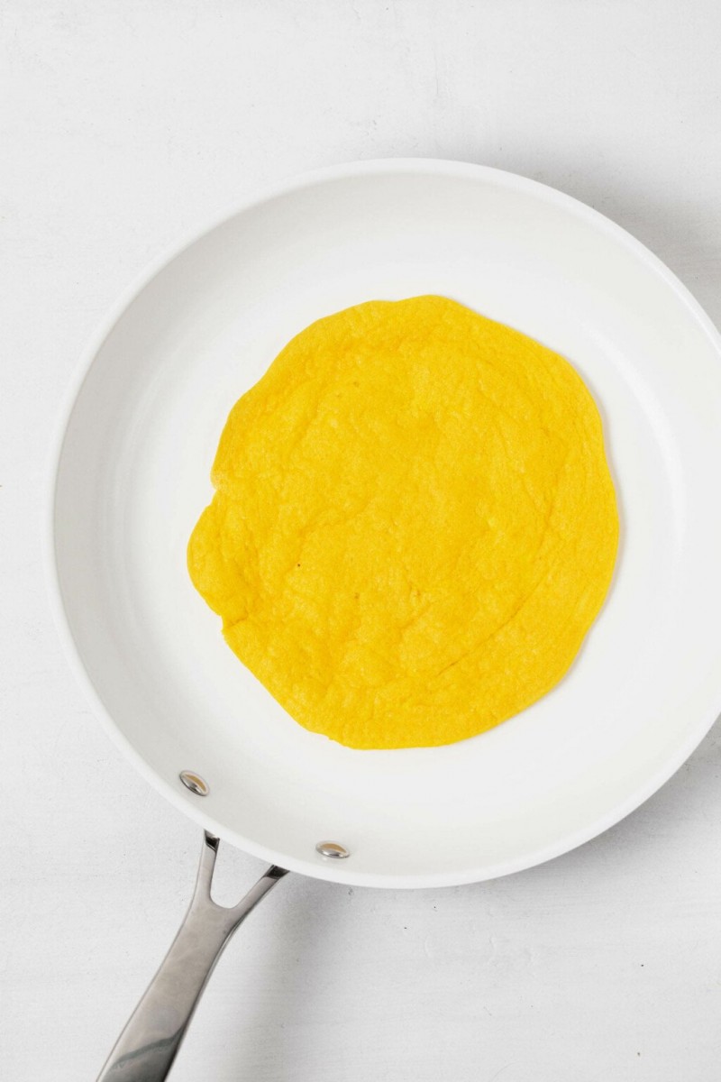 A small, white nonstick skillet is being used to flip a plant-based egg mixture.