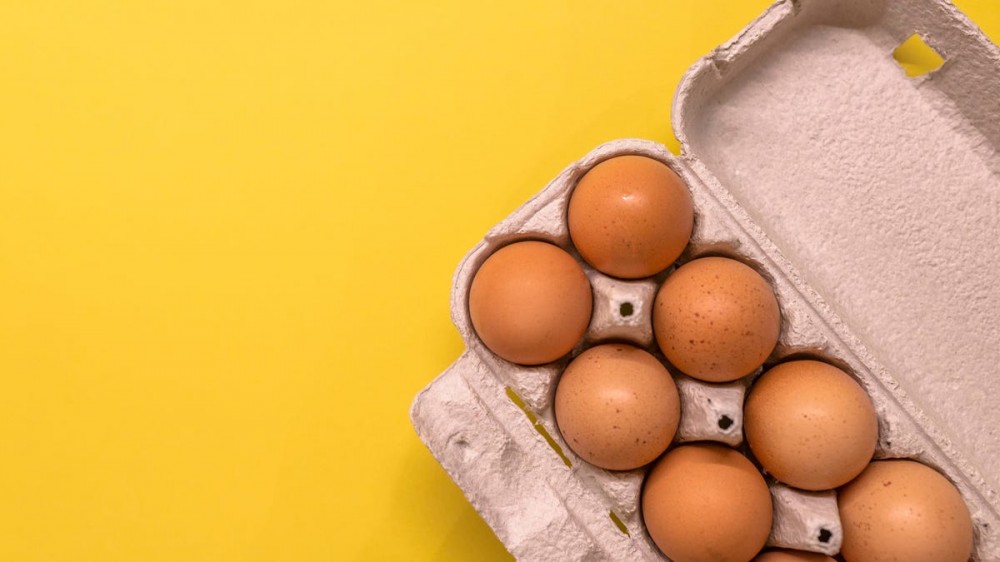 A carton of eggs sits on a yellow surface.