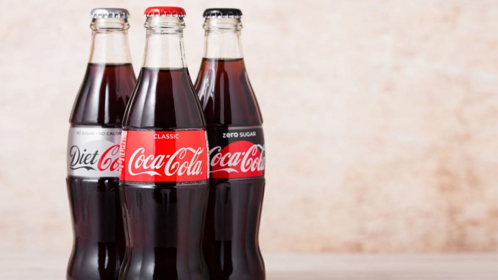 Glass bottles of Coca-Cola, Diet Coke, and Coke Zero sit together.