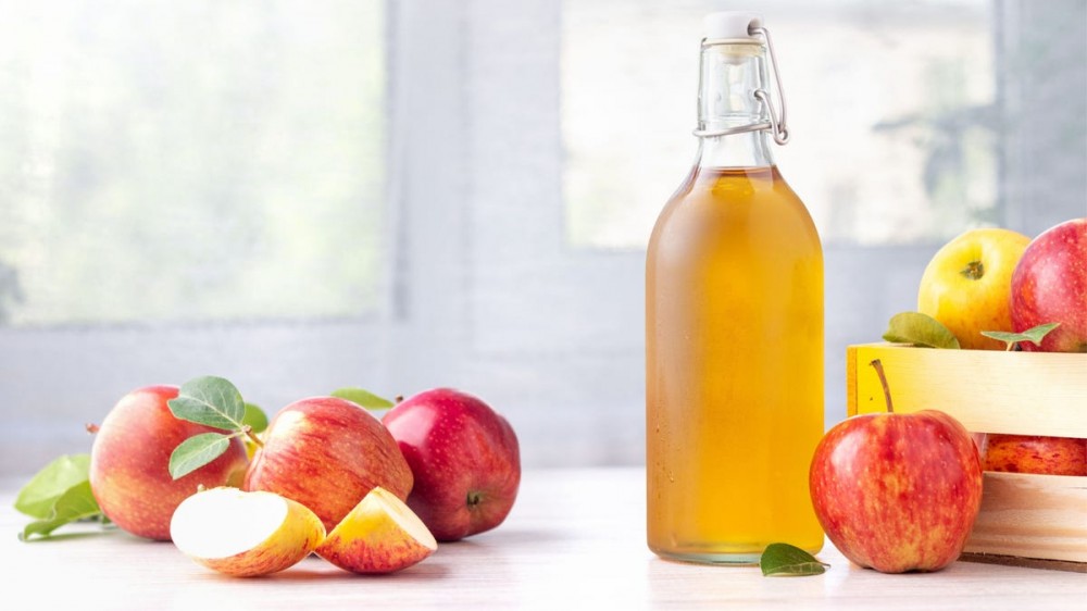 A glass bottle of apple cider is surrounded by apples.