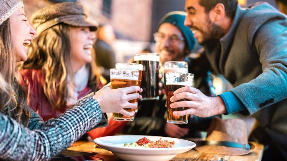 A group of people drink beer outdoors during cold weather.