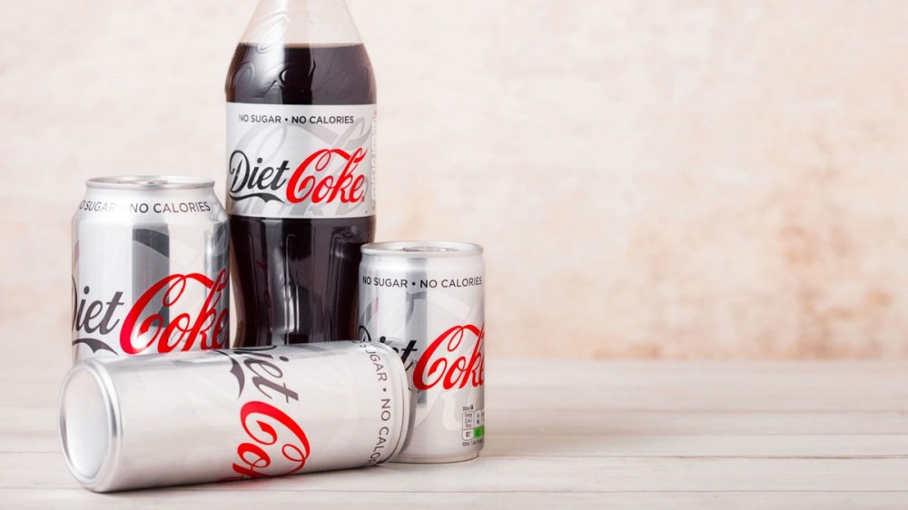 A bottle of Diet Coke sits beside cans of Diet Coke.