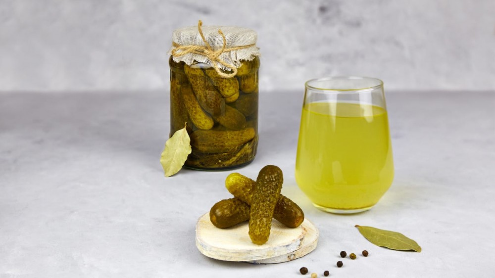 A jar of pickles sits behind a glass of pickle juice and a small plate of pickles.