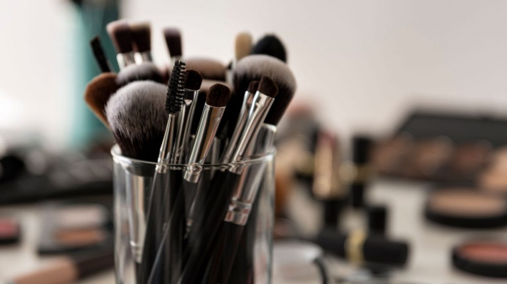 Makeup brushes in a clear holder with makeup in the background.