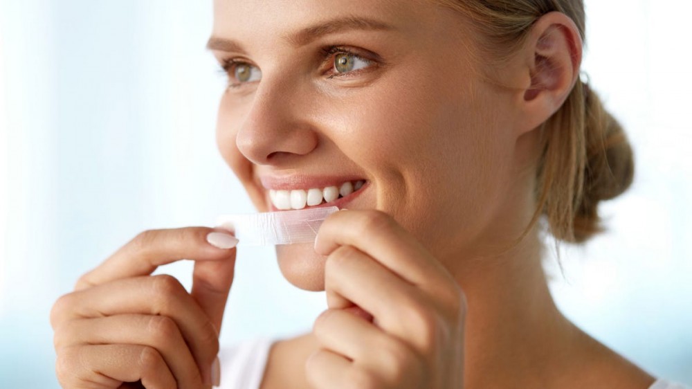 Close-up of woman putting on teeth whitening strips.