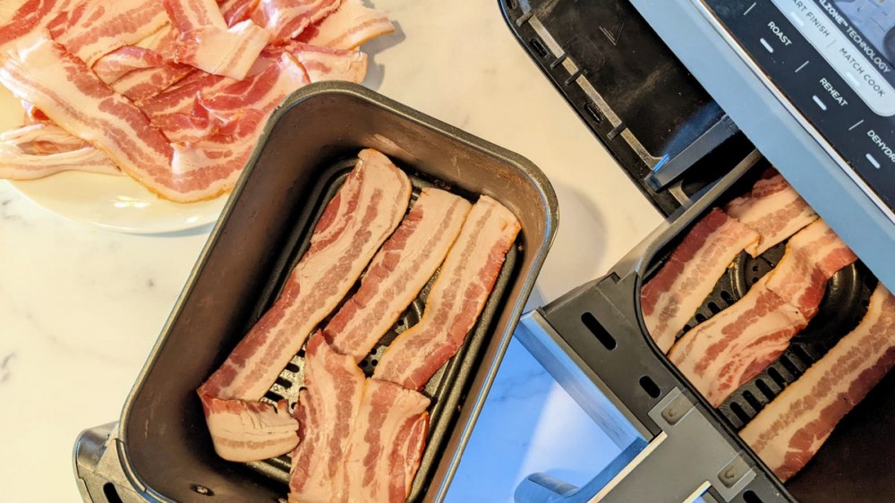 An Ninja Foodie Duel basket air fryer with two baskets filled with raw slices of bacon.