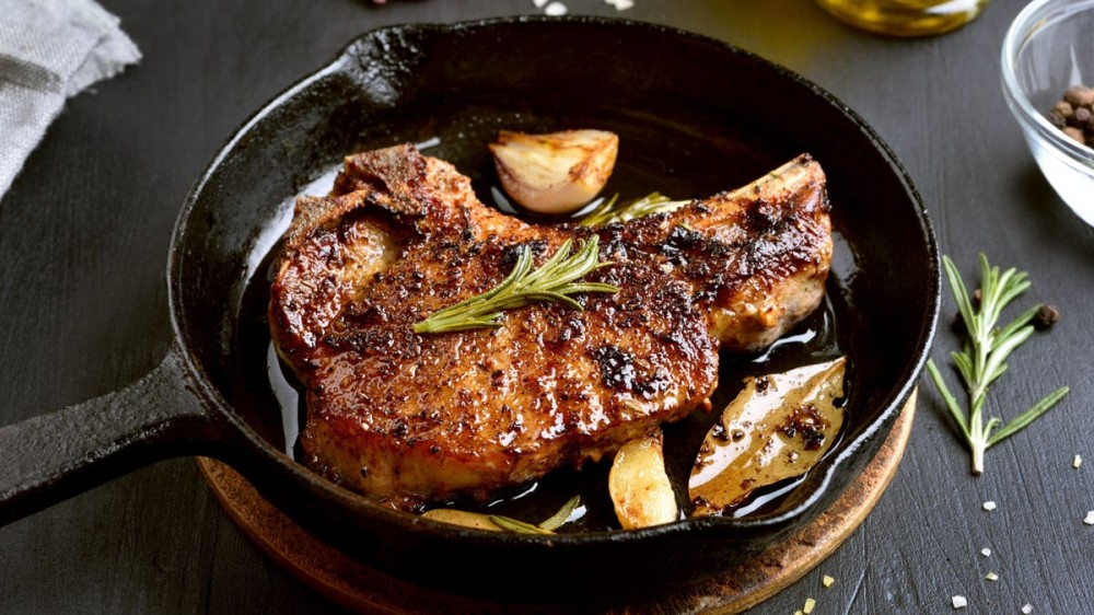 A piece of seared steak in a skillet with rosemary and garlic.