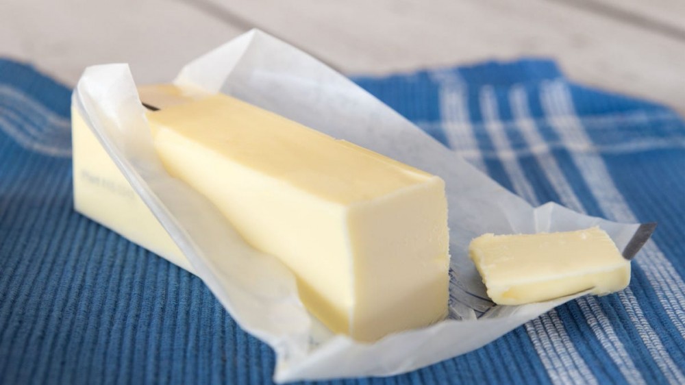 A stick of partially unwrapped butter on a blue kitchen towel.