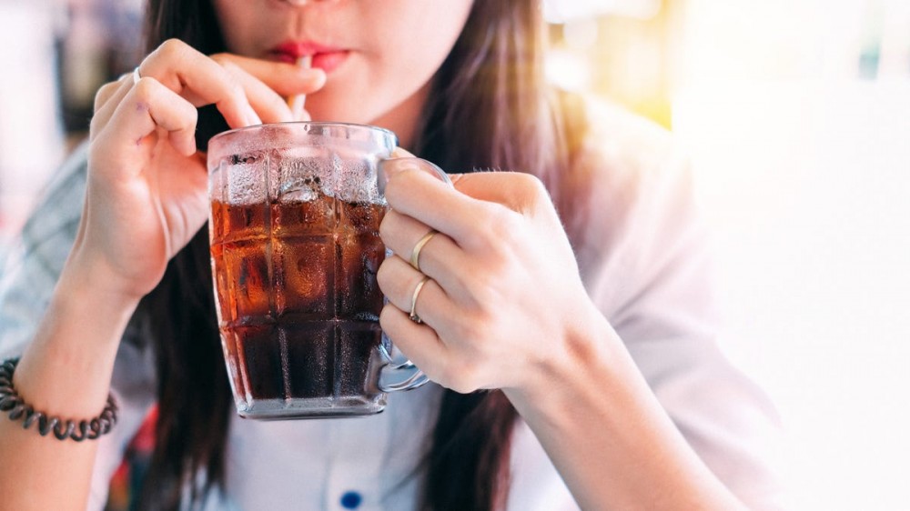 A woman sips a soda from a glass cup.