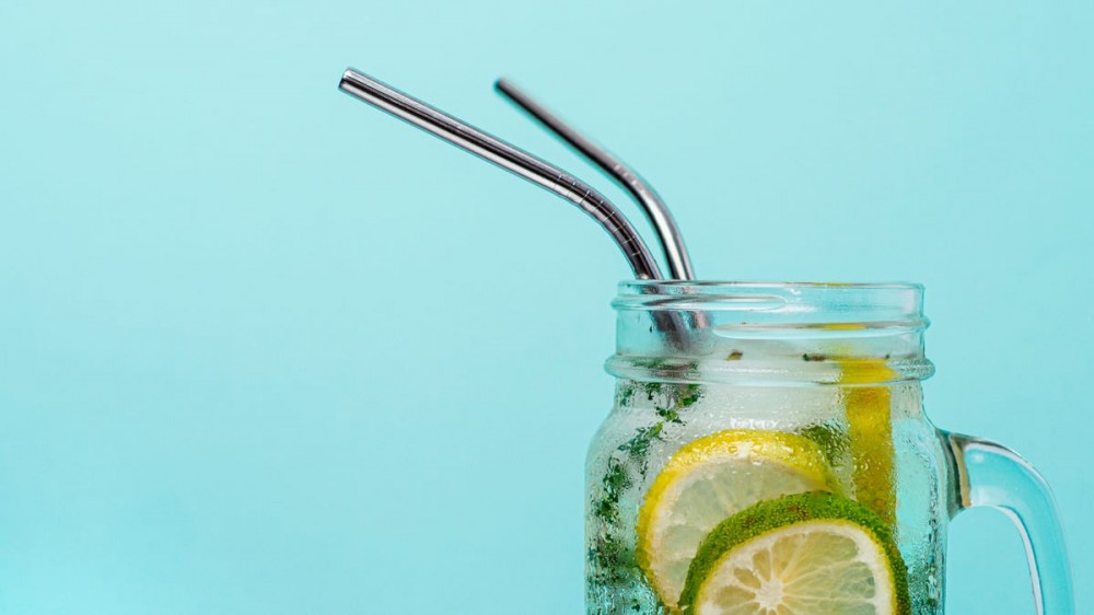 A mason jar is filled with water, lemon, and limes, and two metal straws stick out the top.