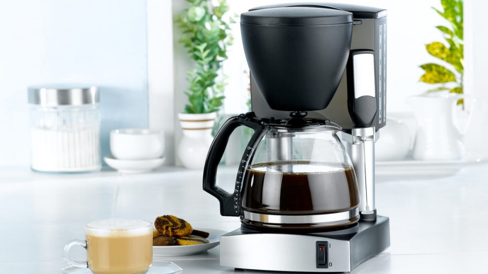 A cup of coffee sits in front of a coffee pot.