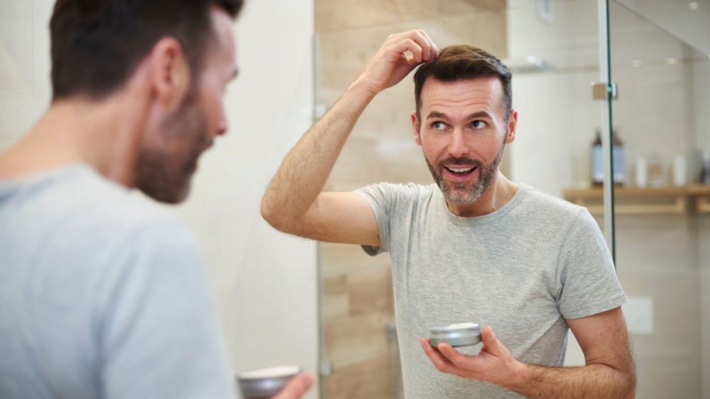 A man applying hair gel in the bathroom.