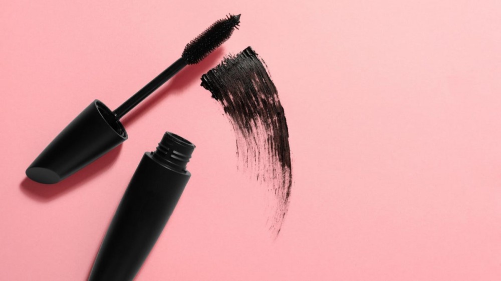 A tube of mascara is swiped over a pink background.