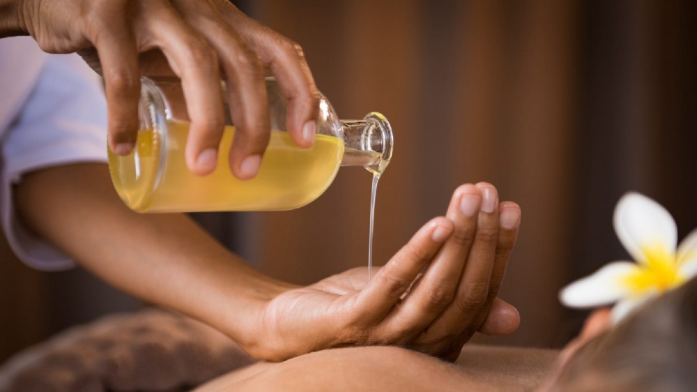 A hand pours body oil from a glass bottle into another hand.