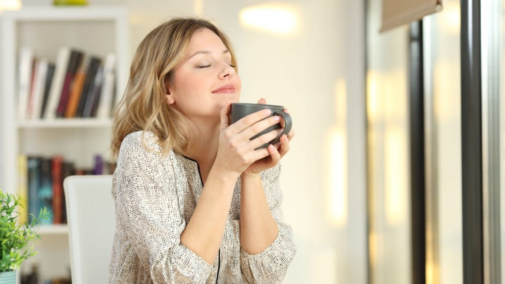 A woman inhales the scent of coffee from a mug.