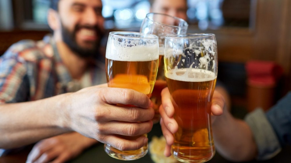 Men cheers with beers in a pint glasses at a bar.