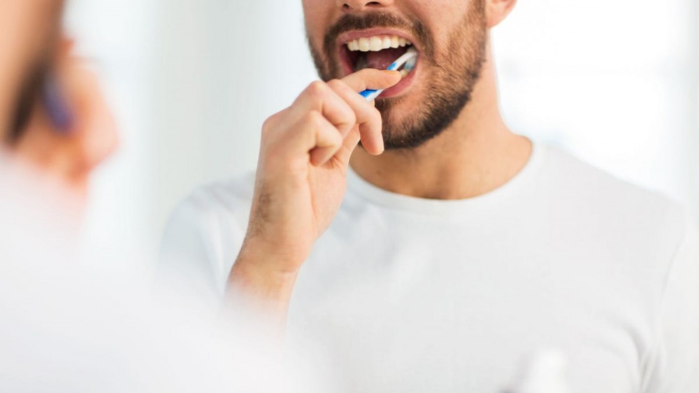 A man brushes his teeth in a mirror.