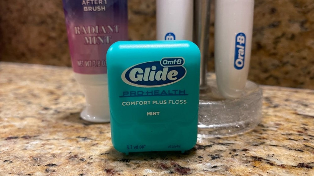 A package of Oral-B Glide Floss is in front of a toothbrush holder and a tube of toothpaste.