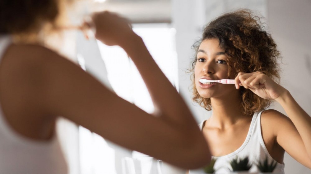 A woman brushes her teeth in front of a mirror.