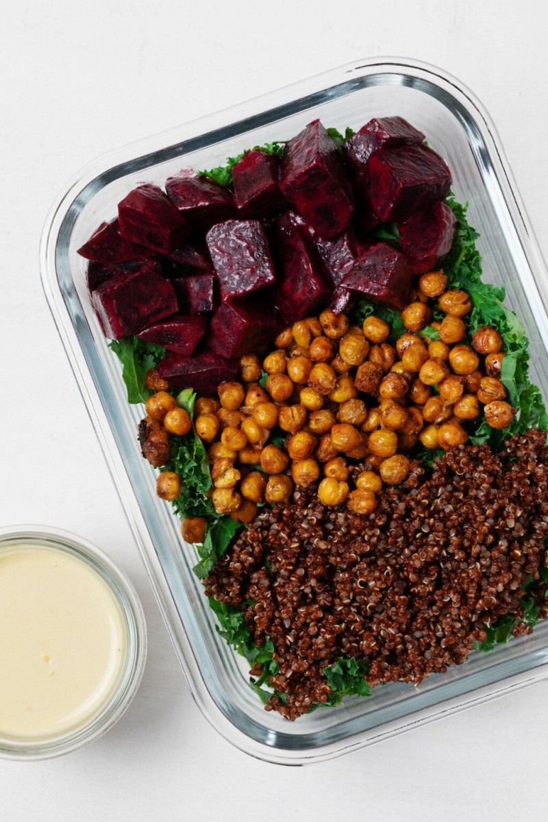 A glass, rectangular storage container holds the components for a plant-based meal, with a small container of dressing nearby.