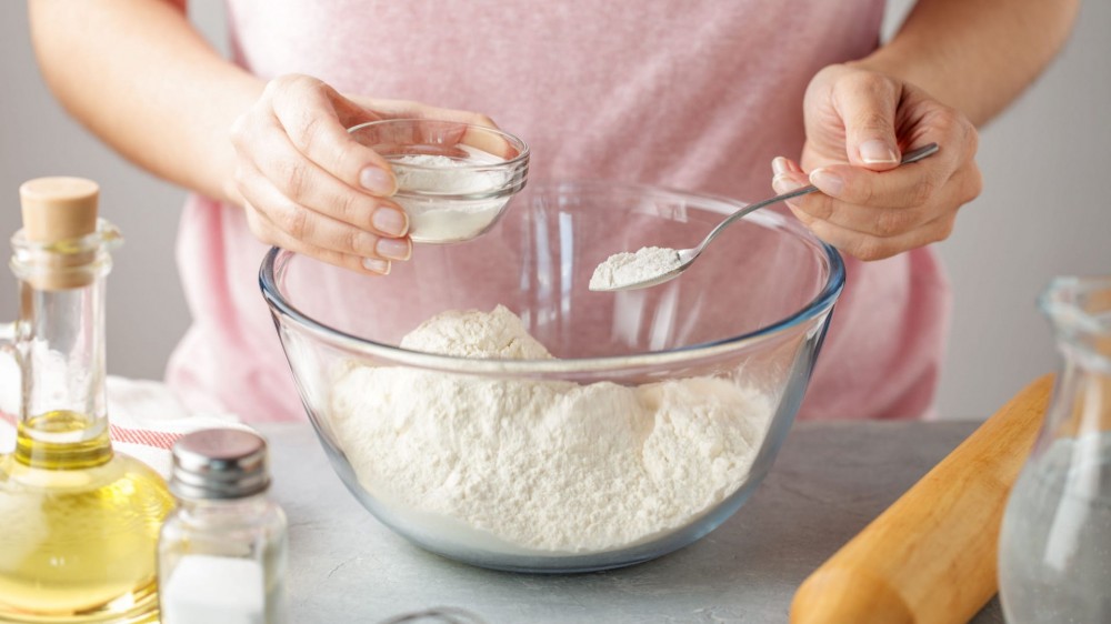 A person adds baking powder to a bowl with flour