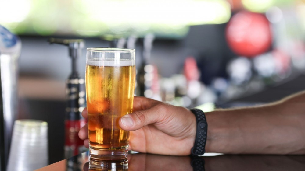 A man holds a pint of beer at a bar.