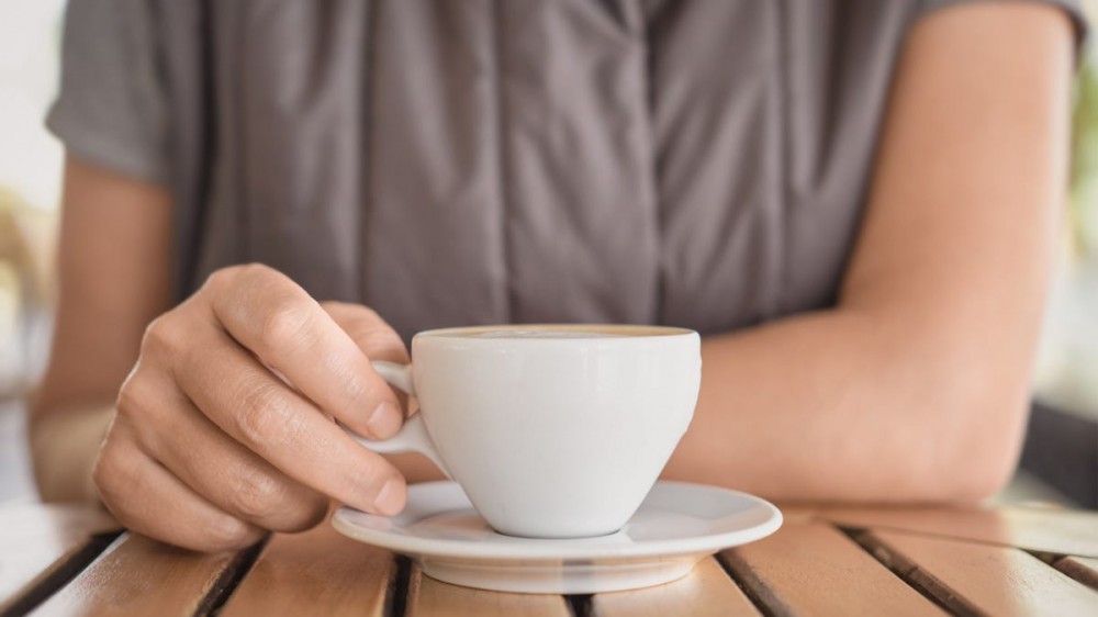 A person sits at a table with a cup of coffee in front of them.