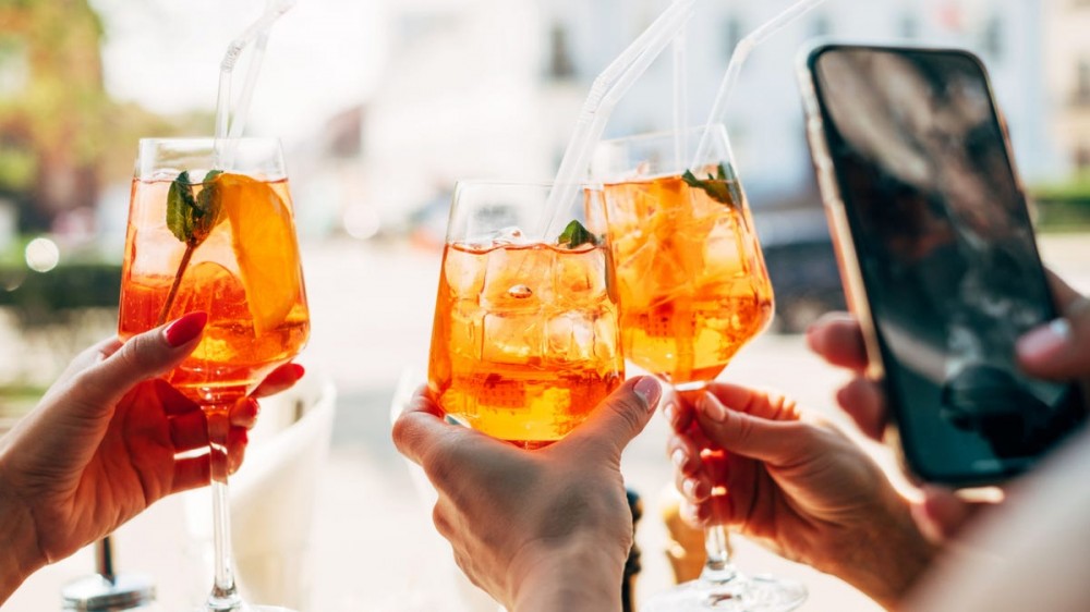 A group of people toast with glasses of aperol spritz.