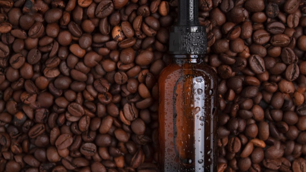 A bottle of serum sits on top of coffee beans.