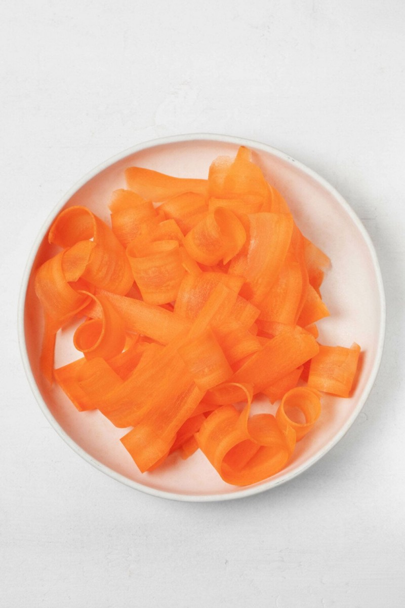 A round, white plate holds shaved ribbons of orange carrot.