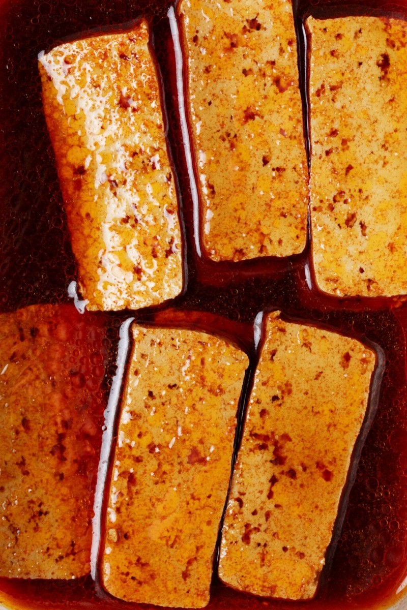 A a close-up image of a dark, liquid marinade, which is being used to season rectangular slices of tofu.