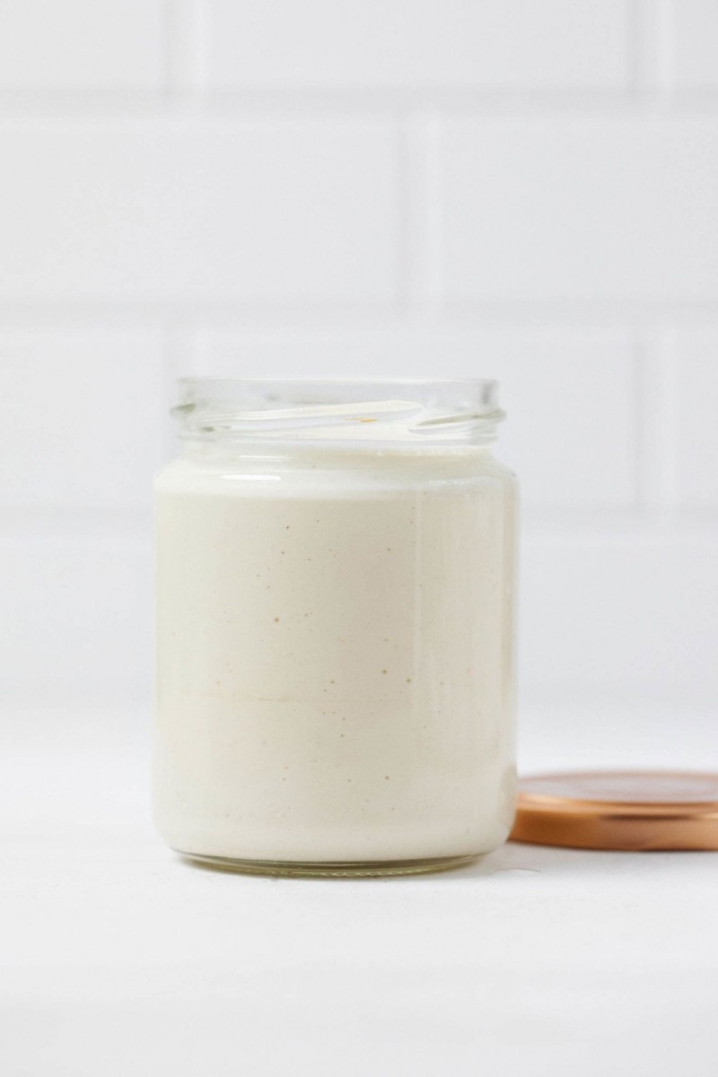 A mason jar has been filled with a vegan mayo, made from cashews. It rests on a white surface.