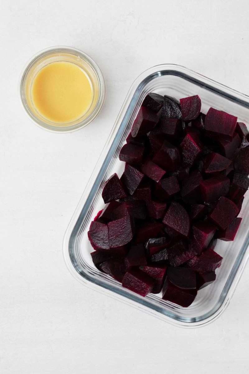 Cut root vegetables are being held in a small, glass storage container with a dressing nearby.