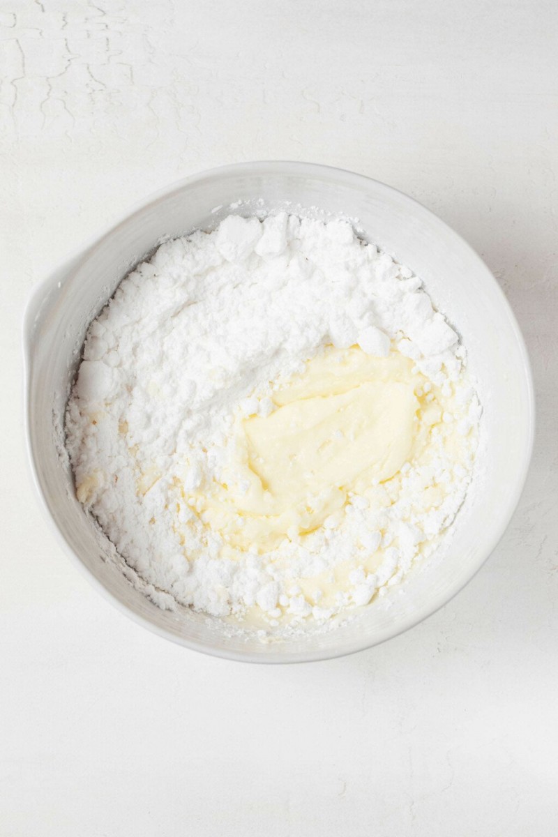 An overhead image of a white bowl, filled with powdered sugar and a creamy base of butter.